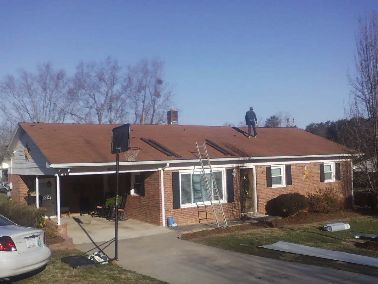 Roofer stripping a shingle roof on a brick ranch before metal panels in Tremont